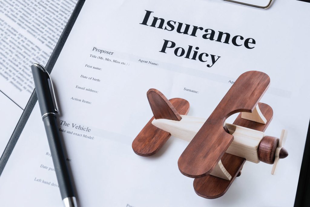 A wooden toy aeroplane and a pen rest on top of an insurance policy document attached to a clipboard, with "Insurance Policy" clearly visible—highlighting the importance of Aviation Cover or Drone Insurance Australia.